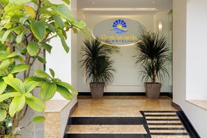 Zona de recepción de un hotel con un letrero que dice Casa Amarilla Hotel, dos plantas en macetas y una escalera de mármol.