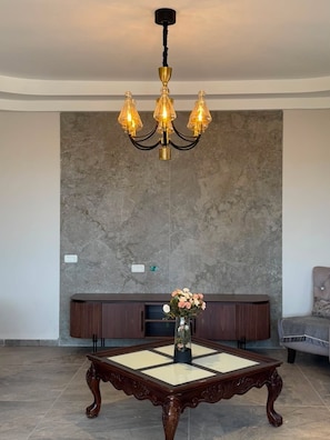 A room with a chandelier, a wooden table with a vase of flowers, and a sofa.