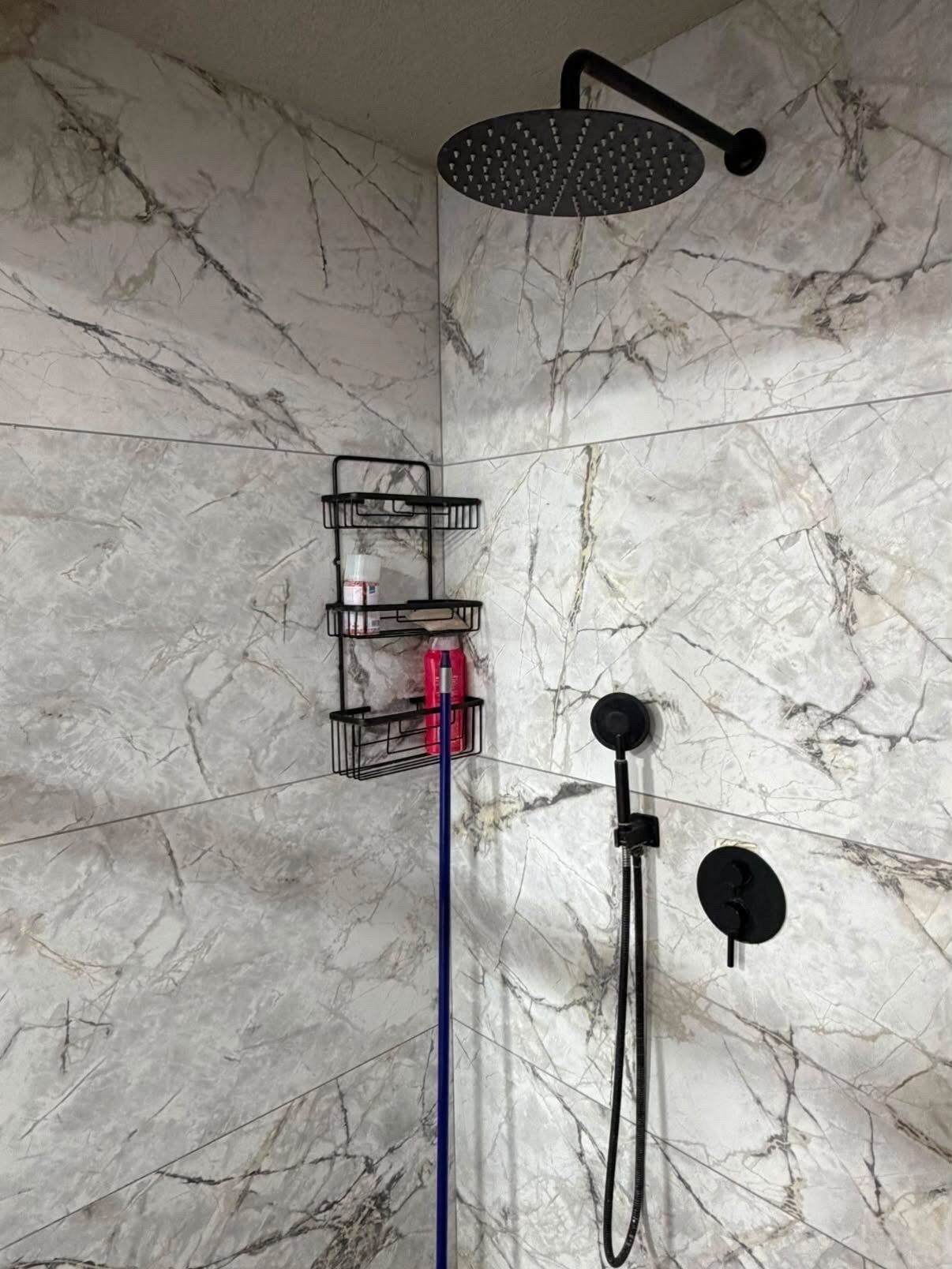 A shower area with a handheld showerhead, a handheld shower attachment, and a wall-mounted shower head.