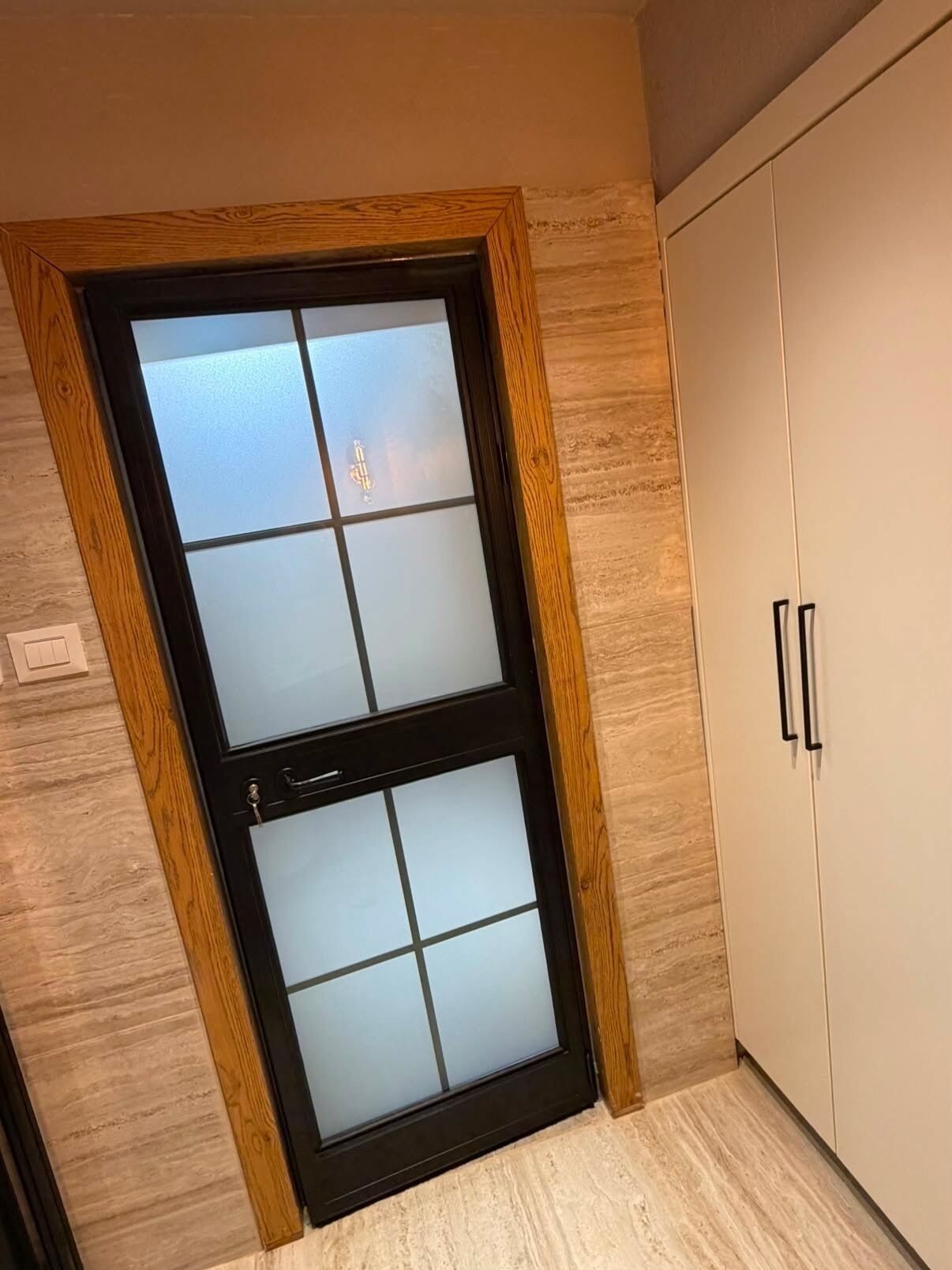 Une pièce avec une porte à cadre en bois, une armoire blanche et un plancher de couleur claire.