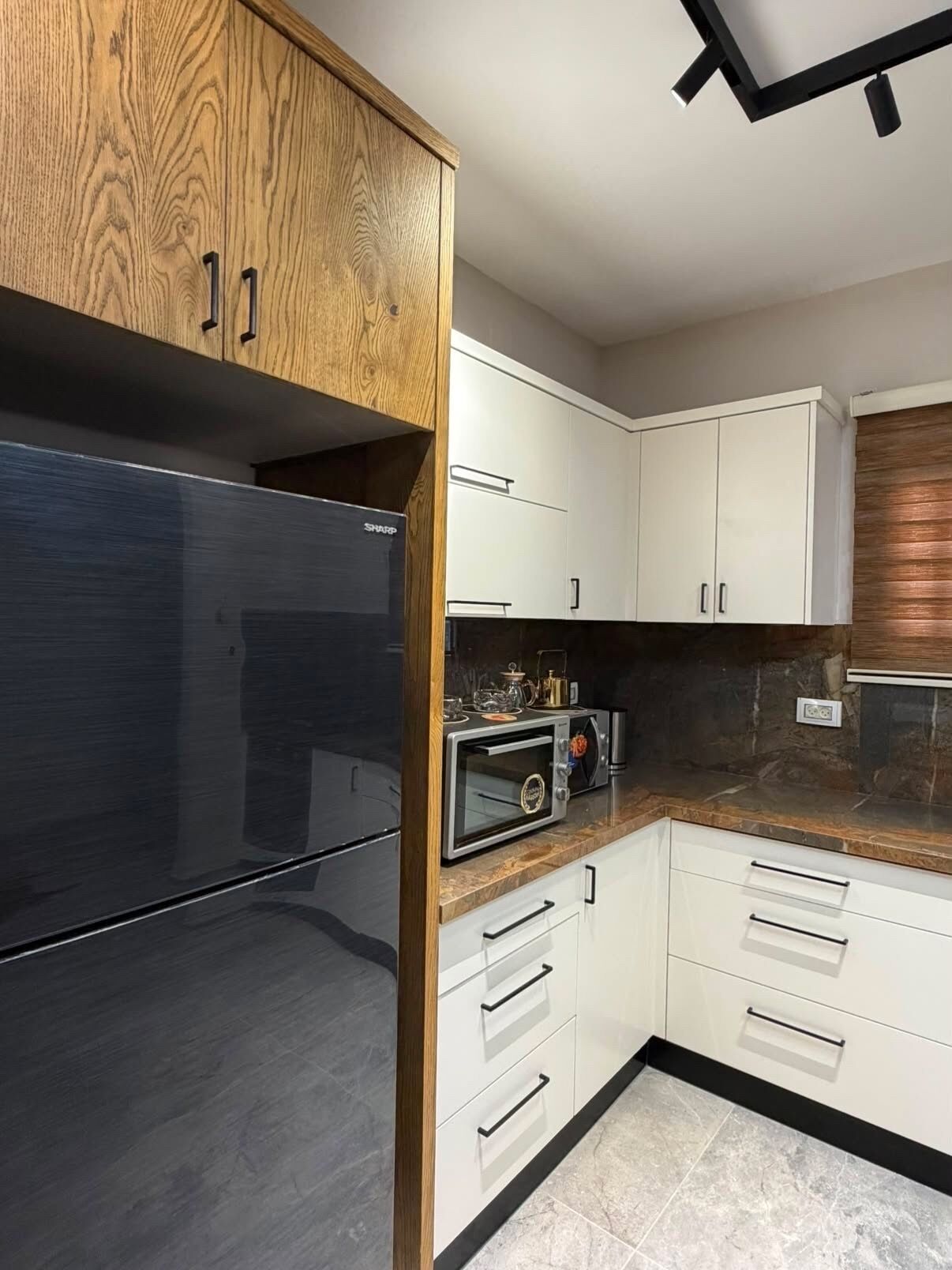 A modern kitchen with a built-in microwave, a stainless steel refrigerator, and wooden cabinetry.