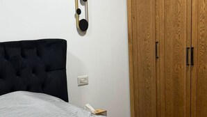 A bedroom with a bed, a wooden wardrobe, and a wall-mounted light fixture.