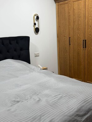 A bedroom with a bed, a wooden wardrobe, and a wall-mounted light fixture.