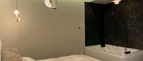 A modern bedroom with a large bed, a built-in bathtub, and a wall-mounted vanity.