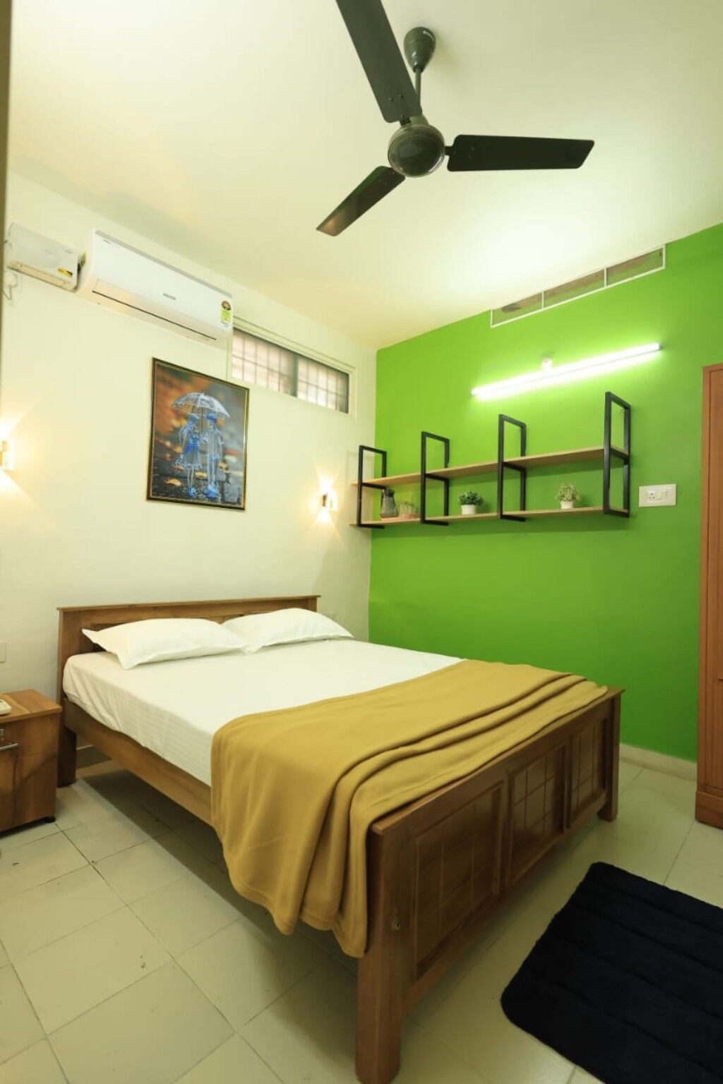 Un dormitorio con cama, ventilador de techo, estante en la pared y un cuadro enmarcado.