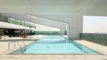 Une piscine sur le toit offrant une vue sur la ville, entourée d’un bâtiment moderne doté de balustrades en verre.