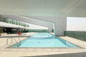 A rooftop swimming pool with a city view, surrounded by a modern building with glass railings. - Elegant 3 BR | Wasl 1 (Dubai)