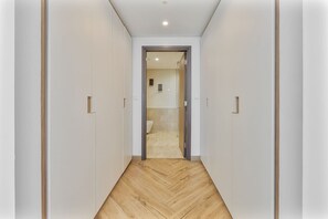 A hallway with a herringbone floor leading to a bathroom with a toilet and a shower. - Elegant 3 BR | Wasl 1 (Dubai)