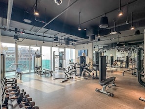 Un gimnasio con equipo de ejercicio diverso, grandes ventanales y vistas a la ciudad.