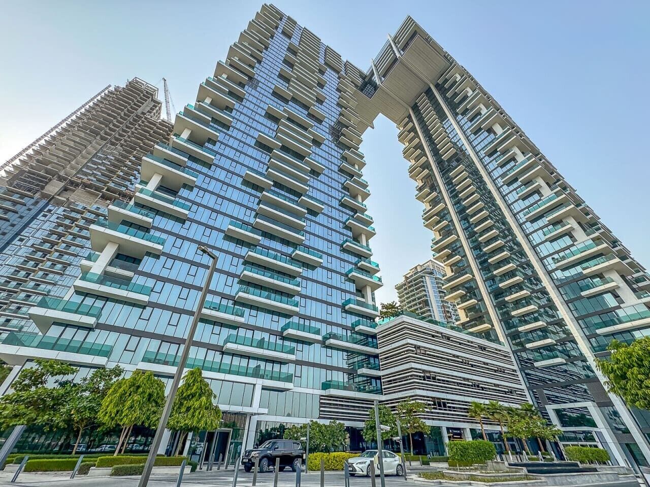 A modern high-rise building with multiple balconies, a glass facade, and a clear sky.