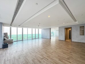 Een ruime kamer met een groot raam, een bank en een deur naar een ander vertrek.