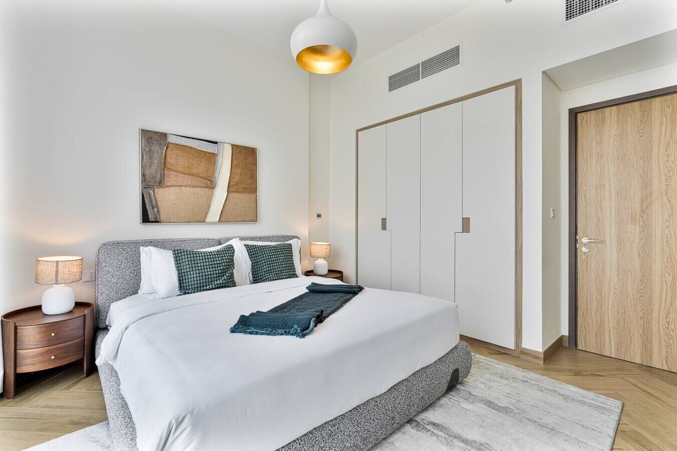 Une chambre moderne comprenant un lit, des tables de chevet, un luminaire suspendu, une armoire et une porte.