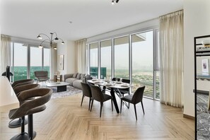A modern hotel room with a dining area, a sofa, and a large window with a city view. - Elegant 3 BR | Wasl 1 (Dubai)