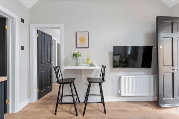 A modern kitchen with a white countertop, two black bar stools, a framed picture of a sun, and a white radiator.