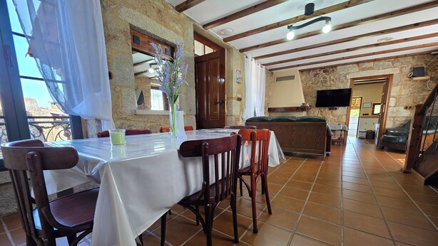 A dining area with a table set for four, wooden chairs, a vase with flowers, and a stone wall.
