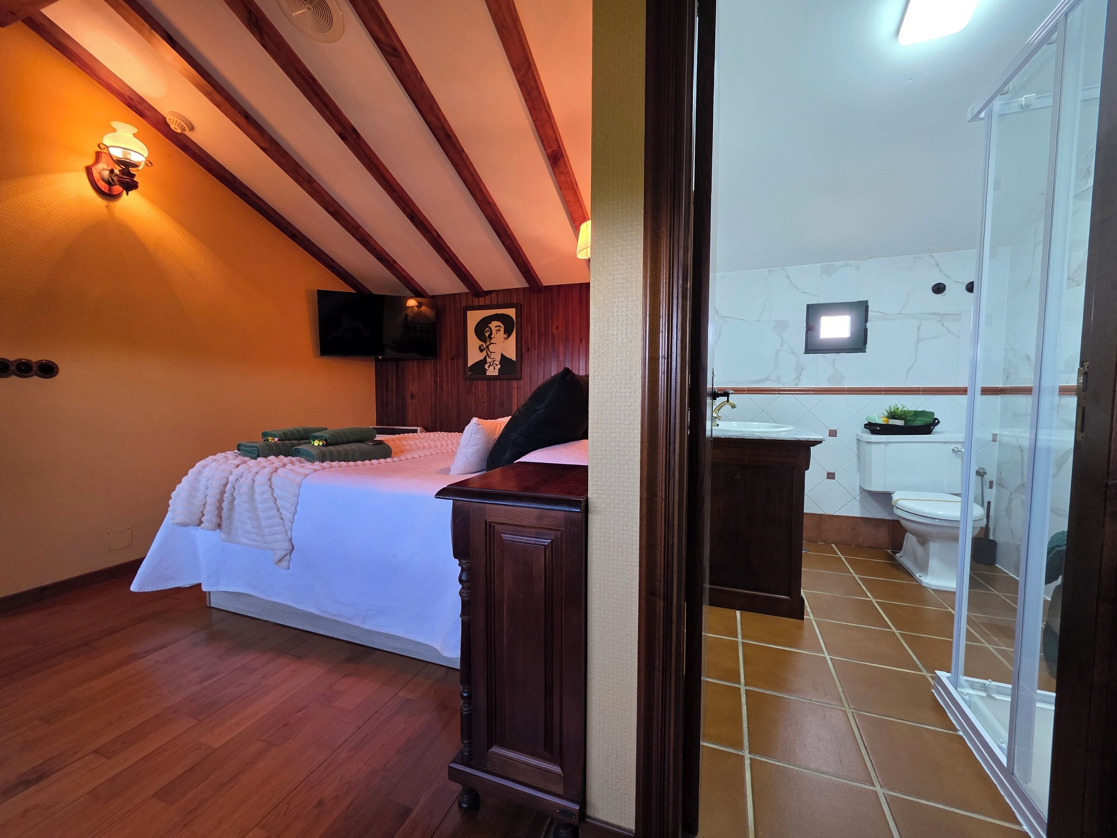 A hotel room with a bed, a wooden dresser, a bathroom with a toilet, sink, and shower.