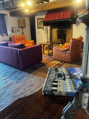 A cozy living room with a fireplace, a purple sofa, patterned armchairs, and a decorative table. - Casa Due - Organic Farmhouse in the heart of Maremma - Paradise for Families (Toscana)