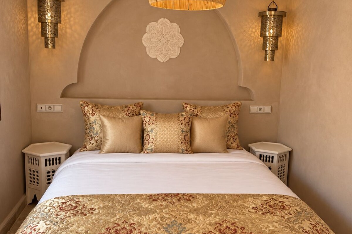 Quarto com cama grande, almofadas decorativas, luminária pendente e luminárias na parede.