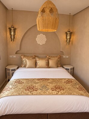 Quarto com cama grande, almofadas decorativas, luminária pendente e luminárias na parede.