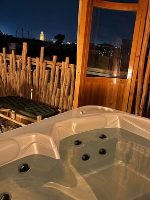 Ofurô com deck de madeira e vista para a cidade à noite.