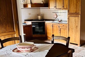 A kitchen with wooden cabinets, a stove, and a dining table with a bowl and saucer. - Casa Uno -Organic Farmhouse Podere Acquarello in the Maremma  - panoramic views. (Toscana)