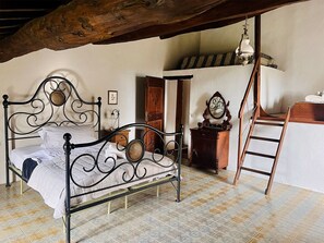 Ein Schlafzimmer mit Metallbettgestell, einer Holzleiter, einem Holzschrank und einer hängenden Deckenleuchte.