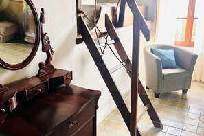 Ein Zimmer mit einem hölzernen Schminktisch, einem Spiegel, einem Sessel mit Kissen und einer Treppe.