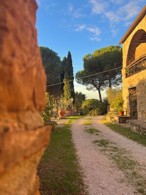 A gravel path leading to a stone building with a balcony, surrounded by trees and potted plants. - Casa Uno -Organic Farmhouse Podere Acquarello in the Maremma  - panoramic views. (Toscana)