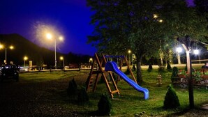 A playground with a slide and swings, surrounded by trees and streetlights.