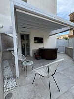 Un patio exterior con un área de estar techada, un jacuzzi y dos sillones de mimbre blanco.