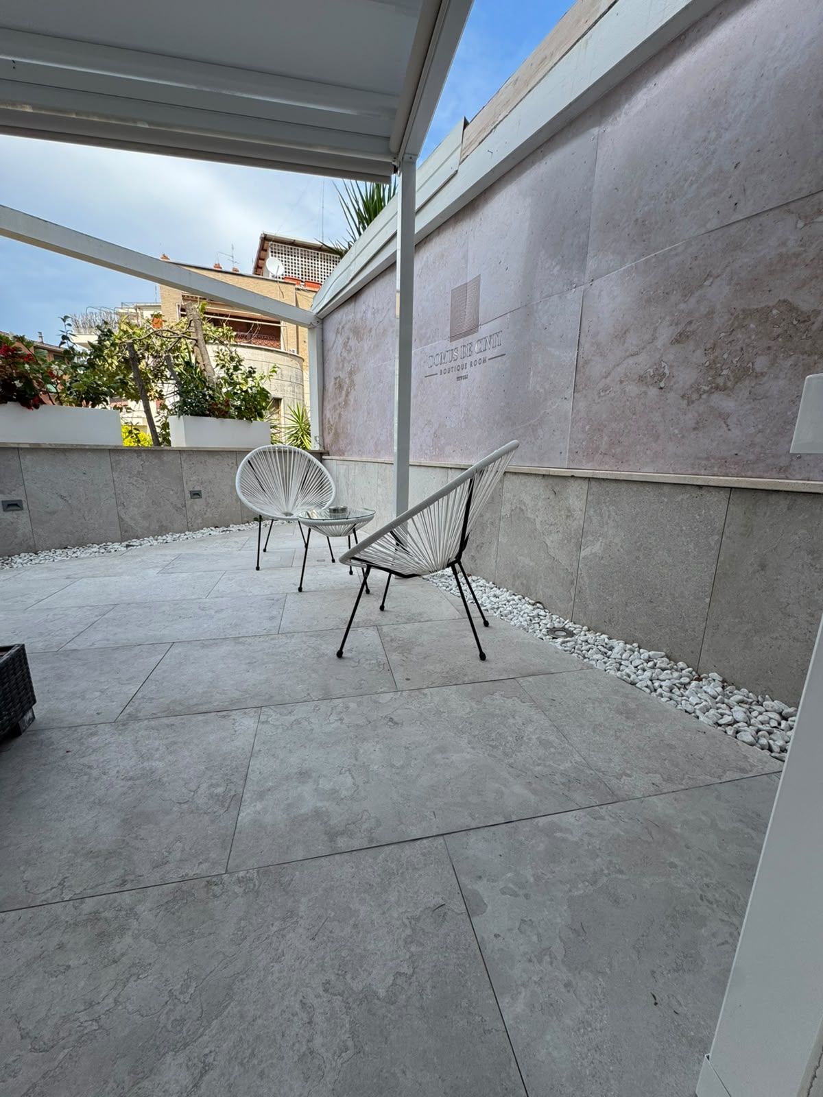 Ein Terrassenbereich im Freien mit einer Sitzecke, einer Wand mit einem Schild und Blick auf die umliegenden Gebäude.