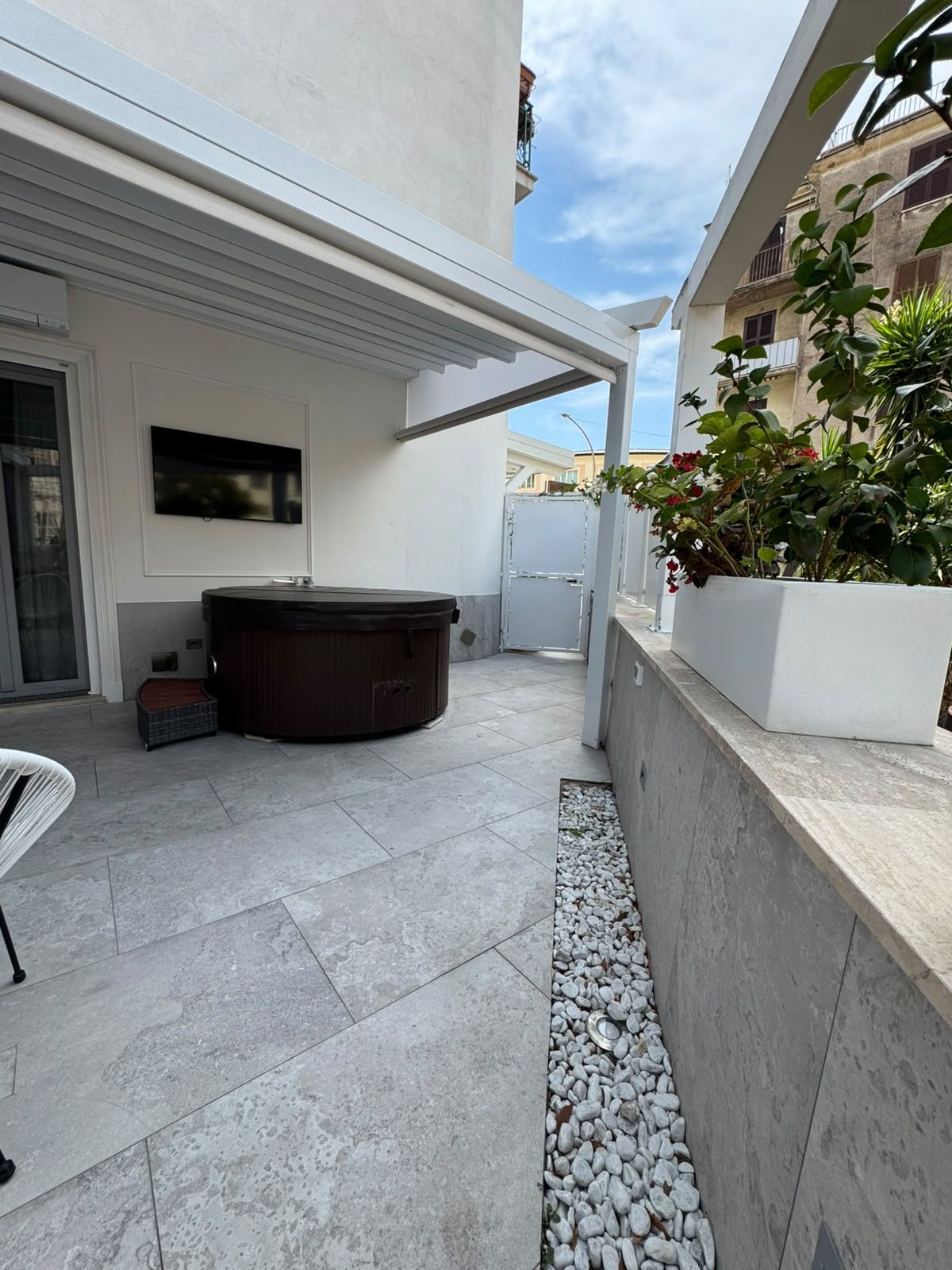 A modern outdoor patio with a hot tub, a seating area, and a white planter with plants.