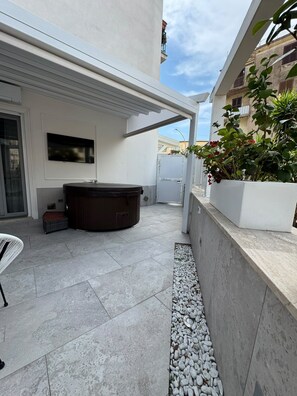 Un patio moderno al aire libre con un jacuzzi, un área de estar y una maceta blanca con plantas.