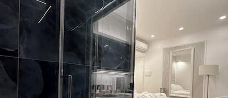 A modern bathroom with a glass shower enclosure, a large mirror, and a white bathtub.