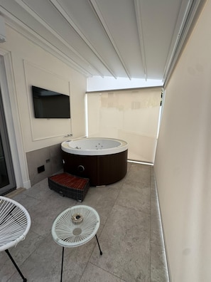 A modern bathroom with a large bathtub, a television, and two white chairs.