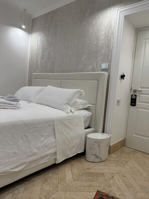 A neatly made bed with a white headboard, a marble nightstand, and a white door with a lock. - Domus De Cinti Boutique Rooms (Tivoli)