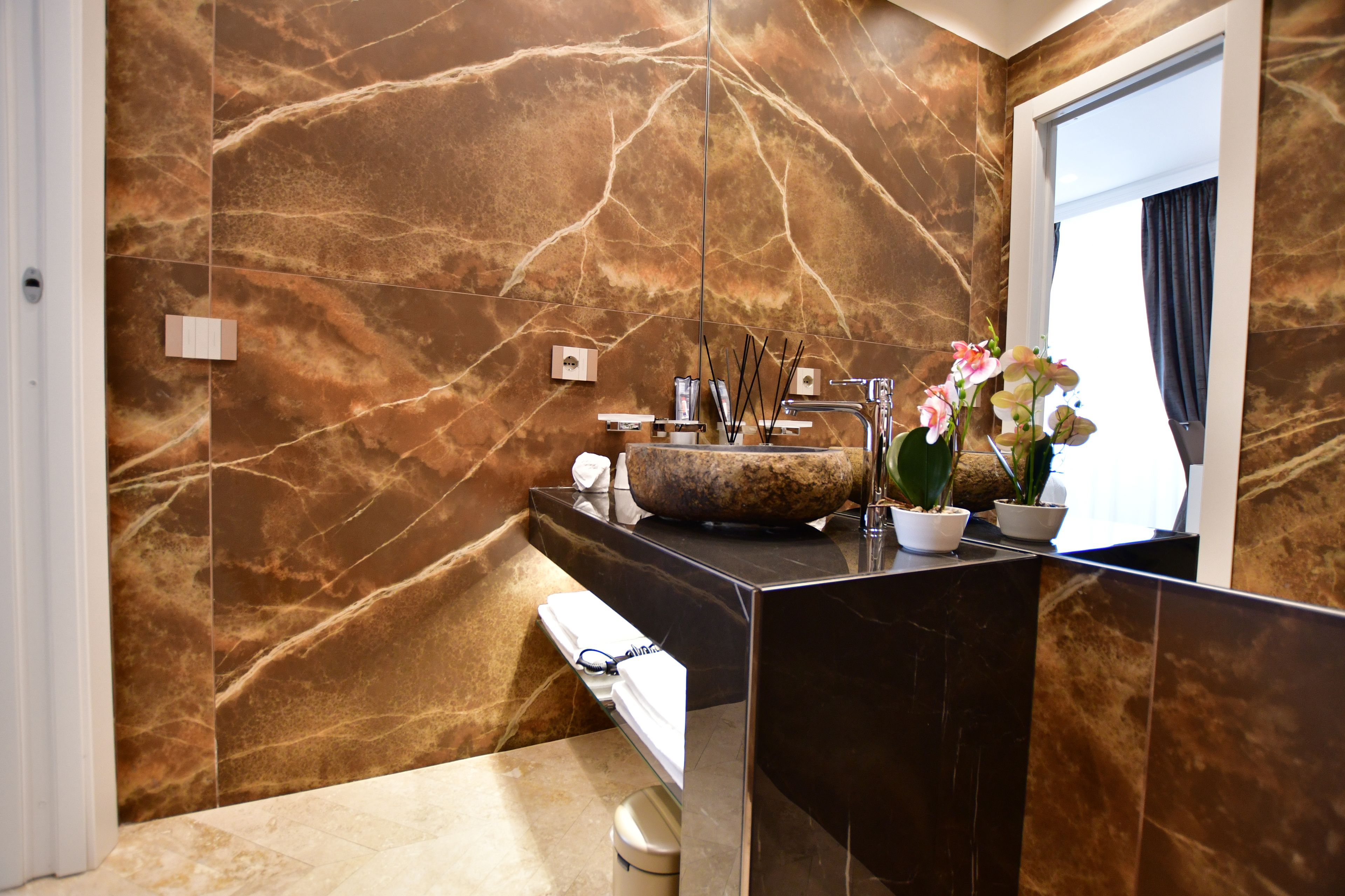 A bathroom with a marble wall, a sink with a stone basin, and a mirror.
