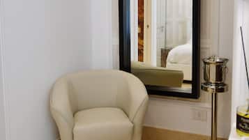 Una habitación con un espejo grande, un sillón color beige, una lámpara de pie y una mesita con una botella.