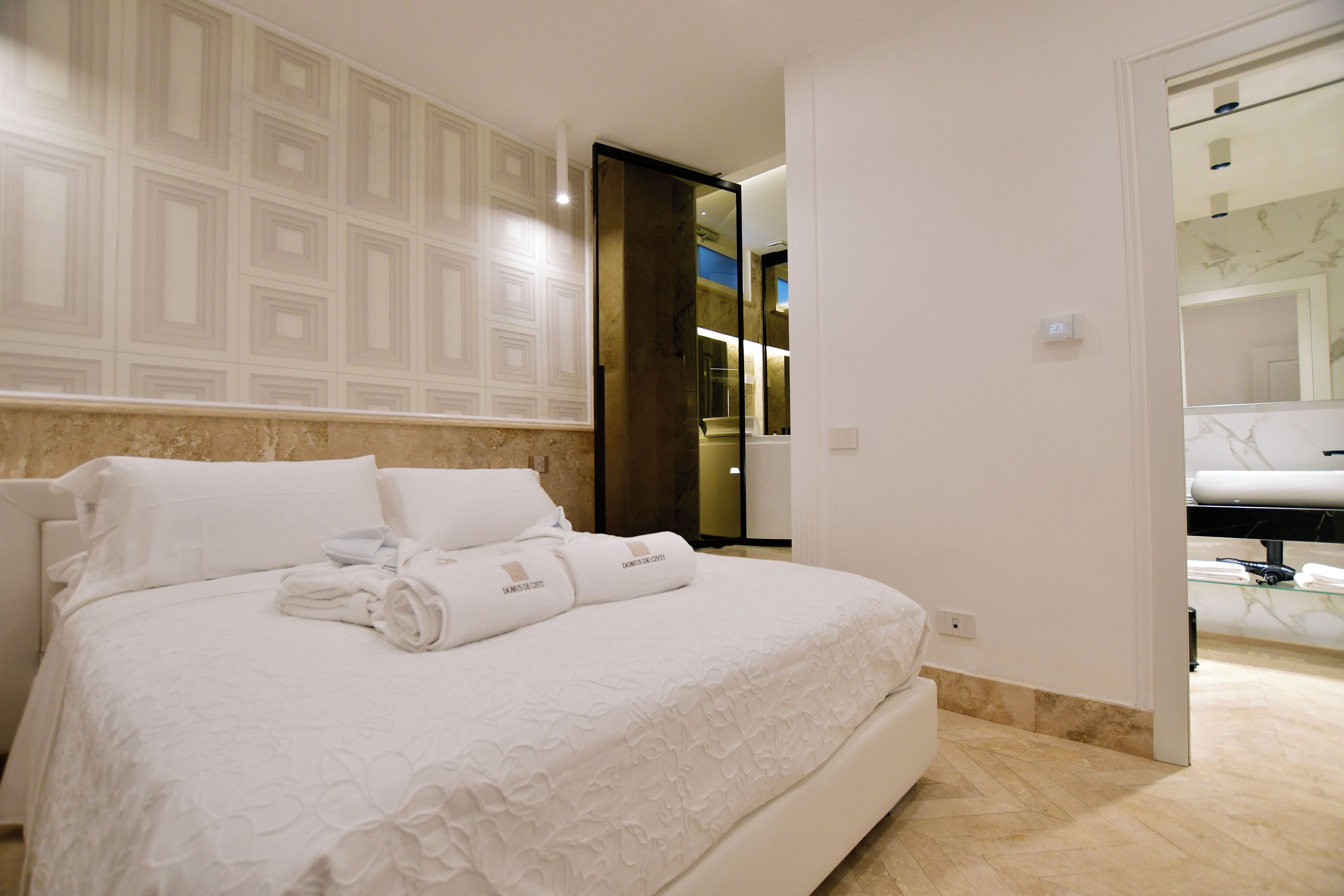 A hotel room with a large bed, a bathroom with a mirror, and a door leading to another room.