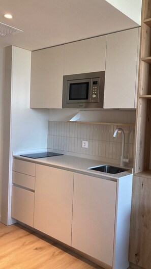 Een kleine keuken met een ingebouwde magnetron, een spoelbak en een aanrecht.