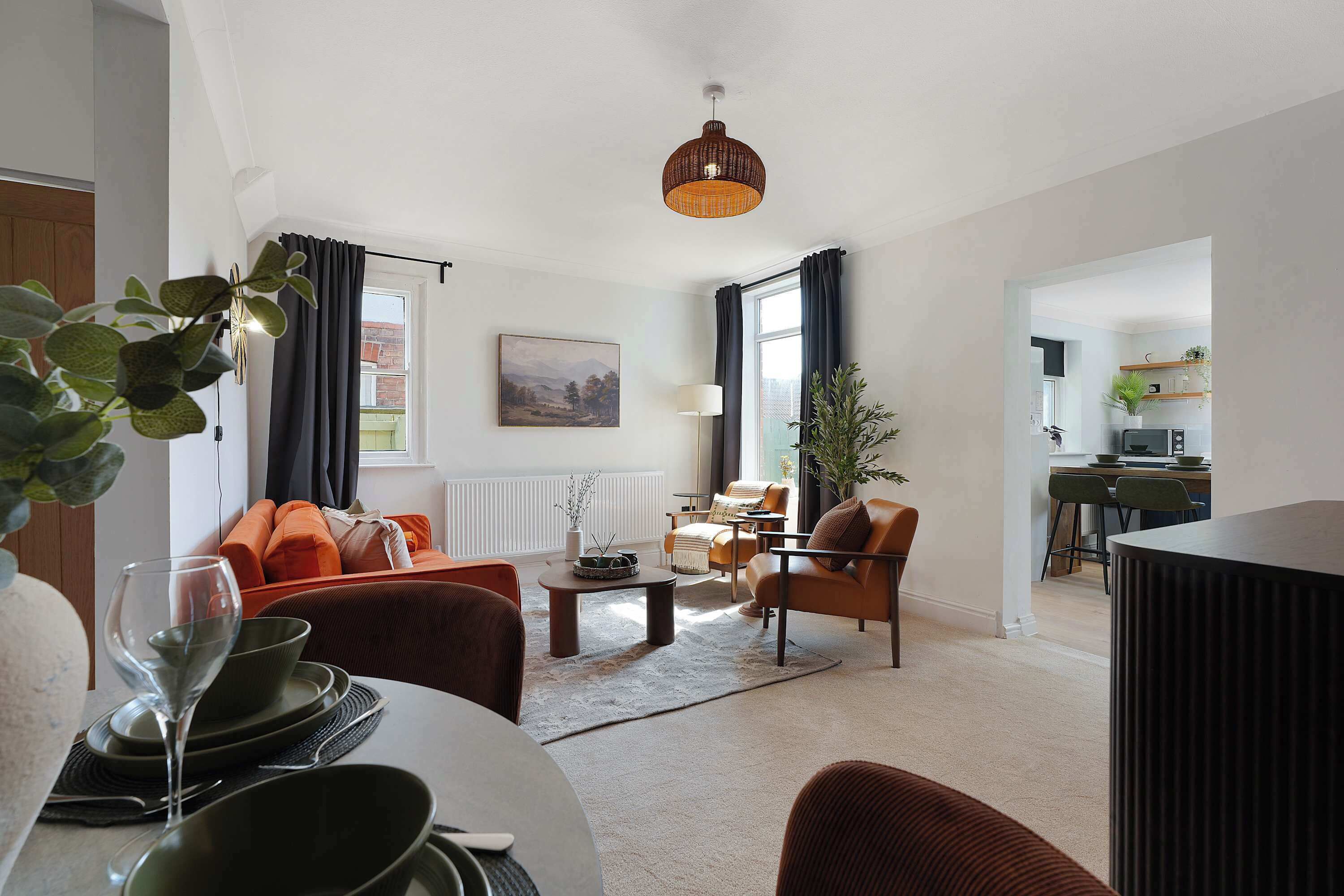 Een moderne woonkamer met een bank, fauteuils, een salontafel en een eethoek met een tafel gedekt voor twee personen.