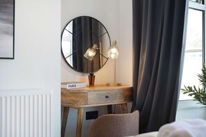 Ein Zimmer mit einem Nachttisch aus Holz, einem runden Spiegel und zwei Wandleuchten.