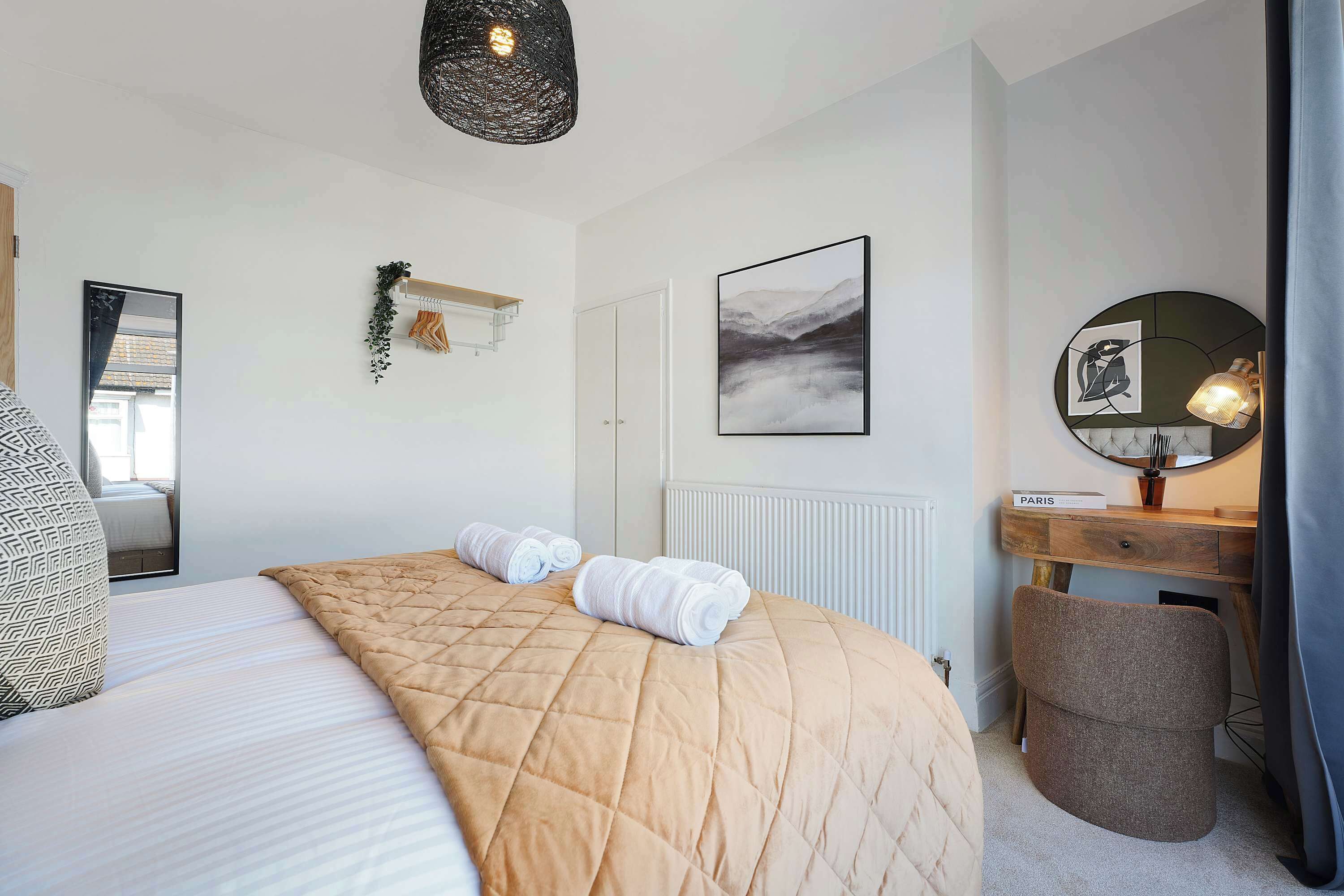 A bedroom with a bed, a bedside table, a mirror, a wall-mounted artwork, and a hanging light fixture.