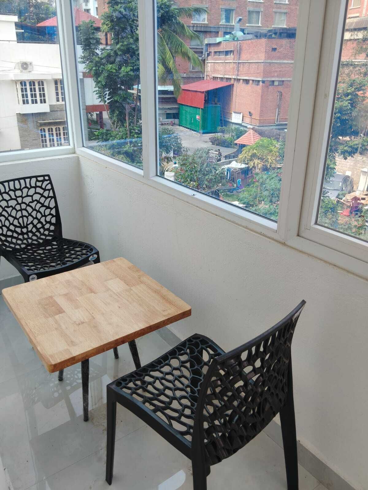 Un balcón con una mesa de madera y dos sillas, con vistas a una zona residencial con edificios y zonas verdes.