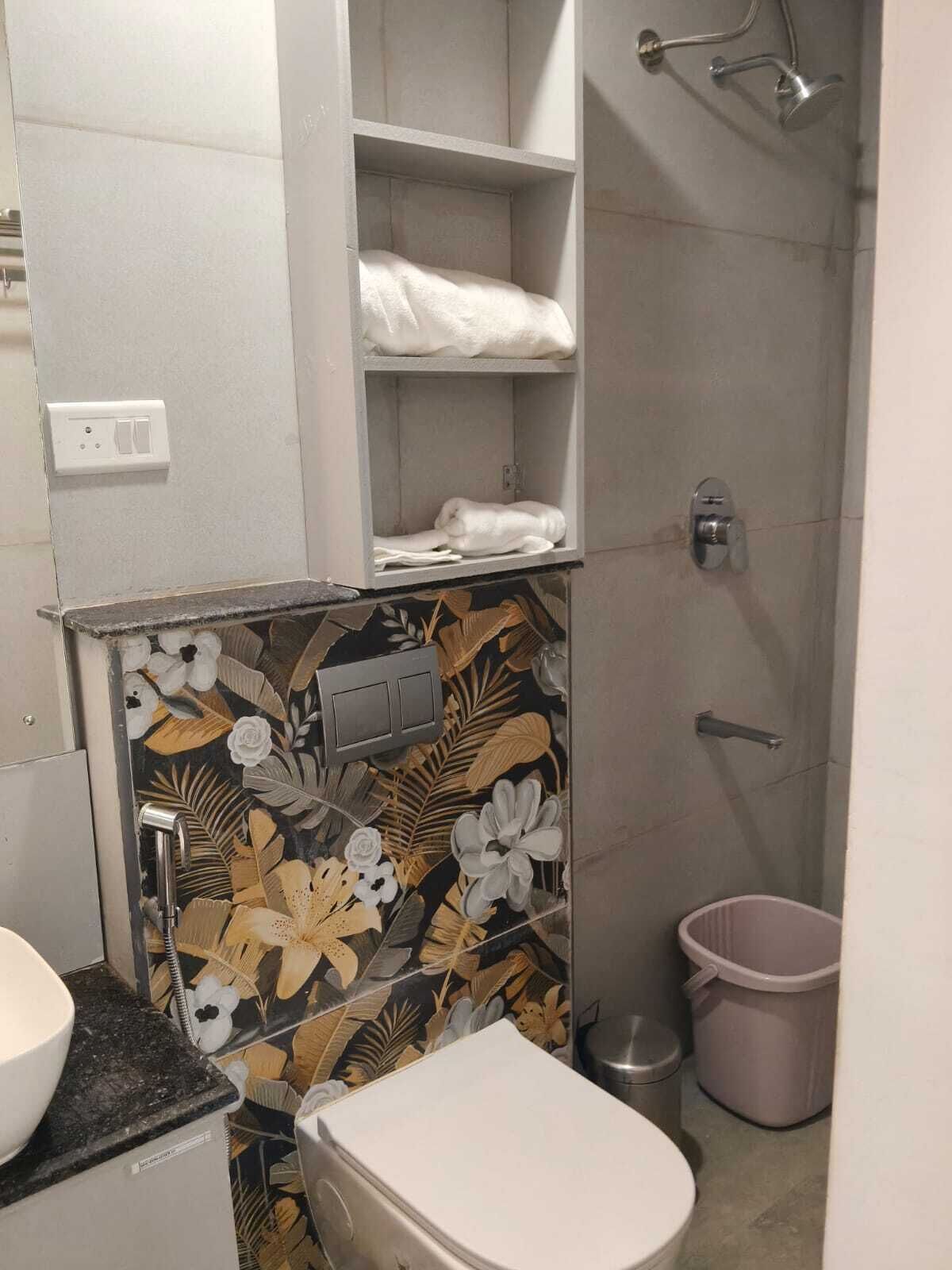 Et badeværelse med toilet, håndvask, bruser og toiletpapirholder.