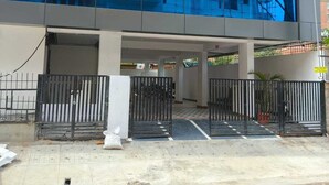 Un edificio moderno con facciata in vetro riflettente, ingresso carrabile e area di parcheggio visibile.