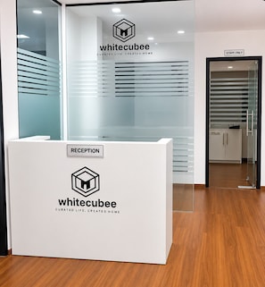 Bancada de recepção com o logotipo 'whitecubee' e a placa 'RECEPTION', que dá acesso a uma área de escritório com paredes de vidro.