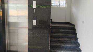 A lift area with a sign 'LIFT-1', a control panel, and a staircase leading to an upper floor.