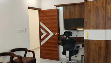 Una habitación con ventilador de techo, una puerta de madera con diseño geométrico, un escritorio con computadora y dos sillas.