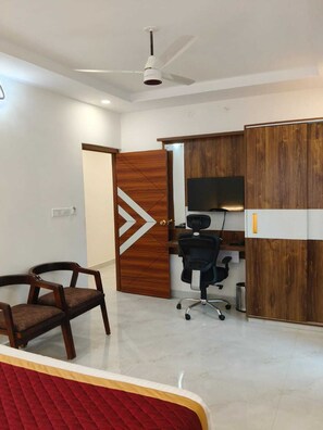 Een kamer met een plafondventilator, een houten deur met een geometrisch ontwerp, een bureau met een computer en twee stoelen.